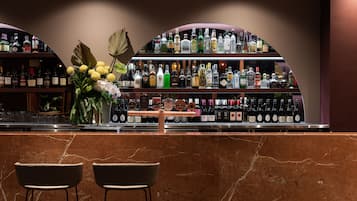 A bar area with a marble counter, two chairs, and shelves stocked with various liquor bottles.