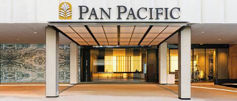The exterior of a Pan Pacific hotel with a modern entrance, a reception desk, and a visible interior through the glass doors.