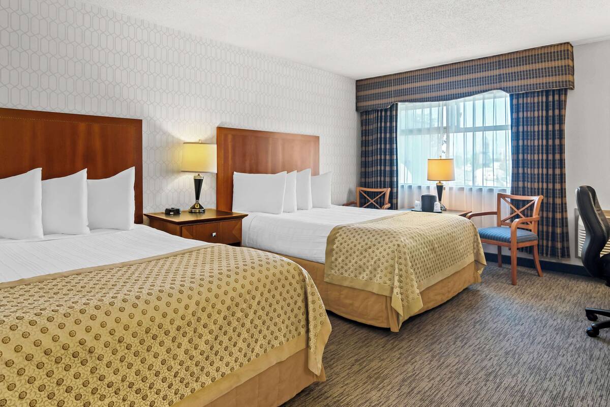 A hotel room with two beds, a desk, a chair, and a window with curtains.
