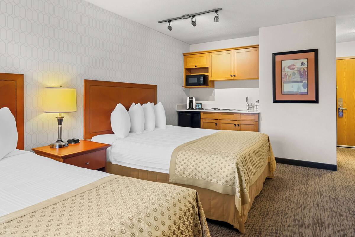 A hotel room with two beds, a kitchenette, and a framed picture on the wall.