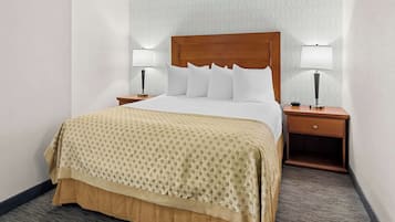A hotel room with a large bed, two bedside tables with lamps, a patterned bedspread, and a carpeted floor.