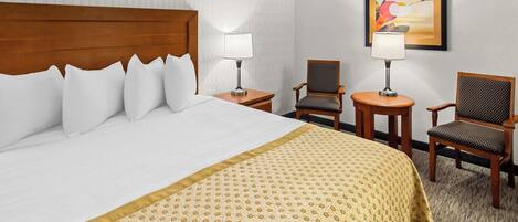 Habitación de hotel con una cama grande, dos sillones, una mesita de noche y una lámpara fijada a la pared.