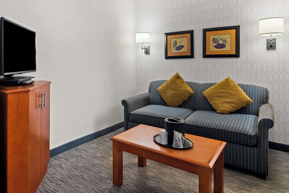 A hotel room with a television on a wooden cabinet, a striped sofa with two pillows, a small table with a cup and saucer, and two wall-mounted lamps.