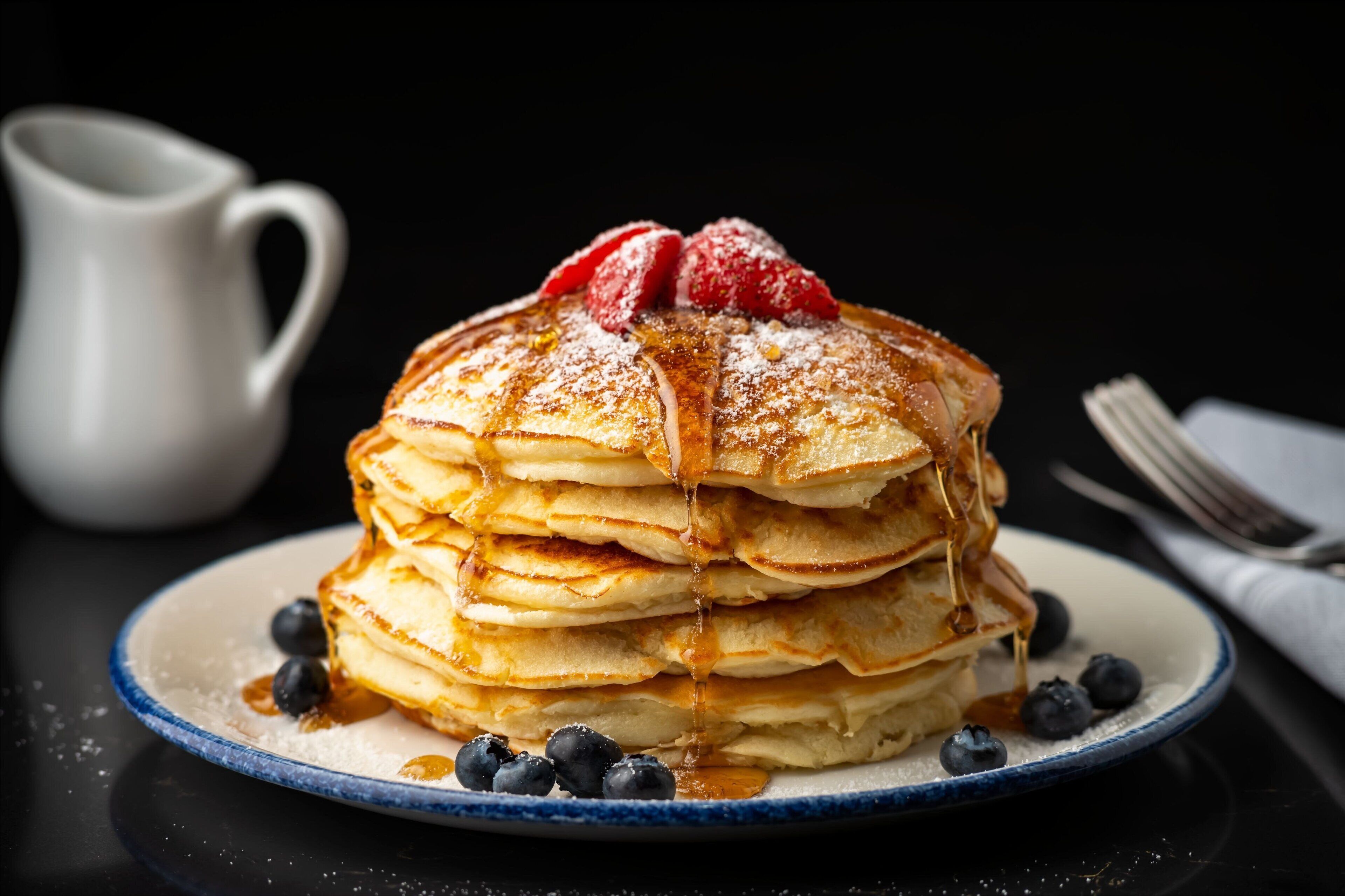 A stack of pancakes with syrup and berries on a plate.