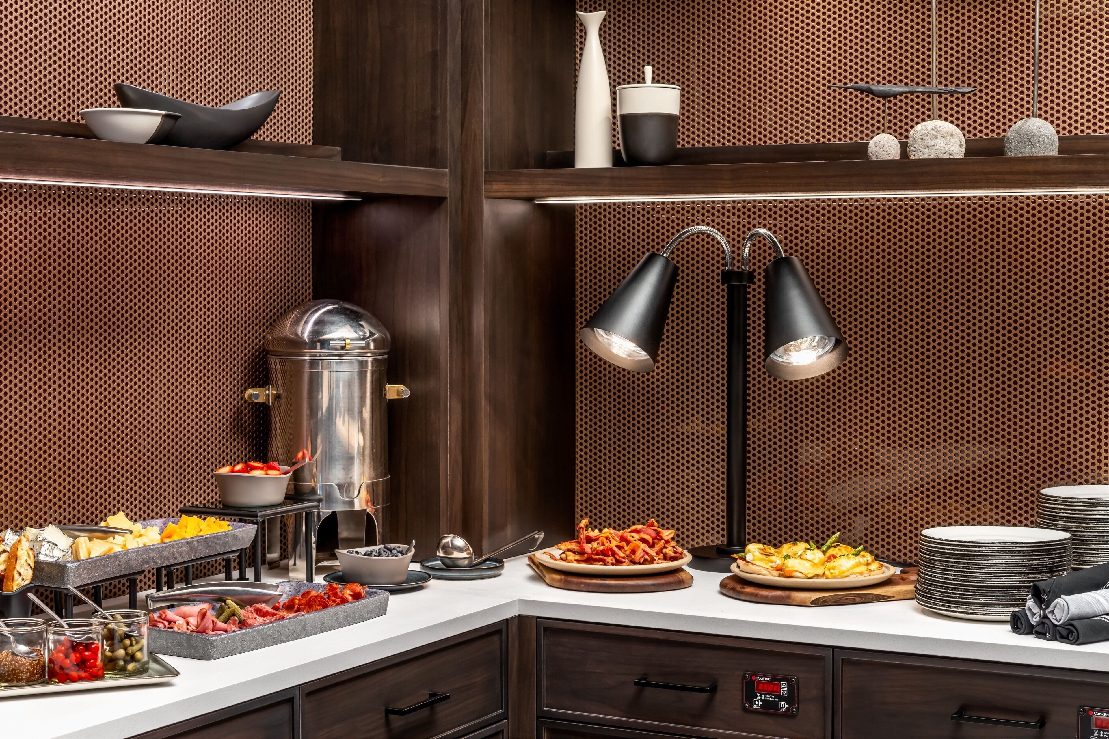 Een buffetopstelling met diverse gerechten, een koffieapparaat en een decoratieve lamp.