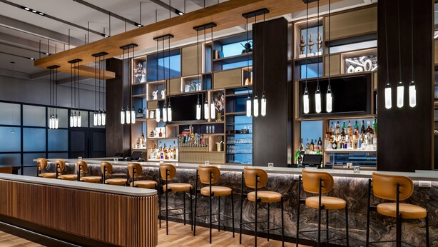 Un espace bar moderne doté d’un long comptoir, de nombreux tabourets et d’une variété de bouteilles et de verres exposés sur des étagères.