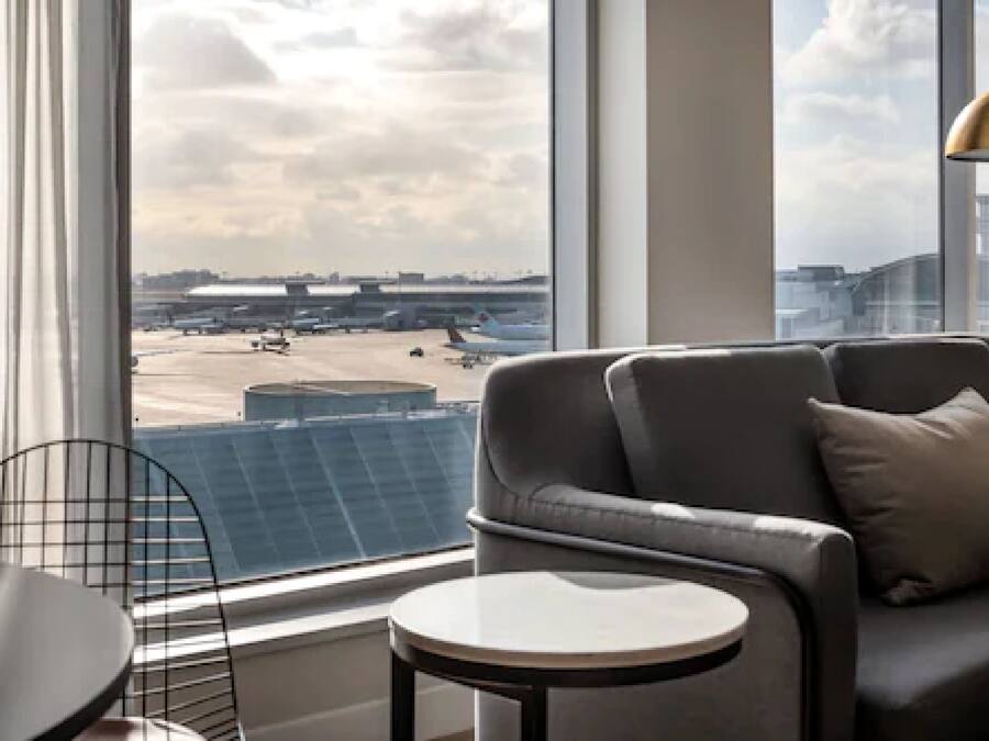Une chambre d’hôtel moderne dotée d’une grande fenêtre donnant sur un aéroport et des immeubles.