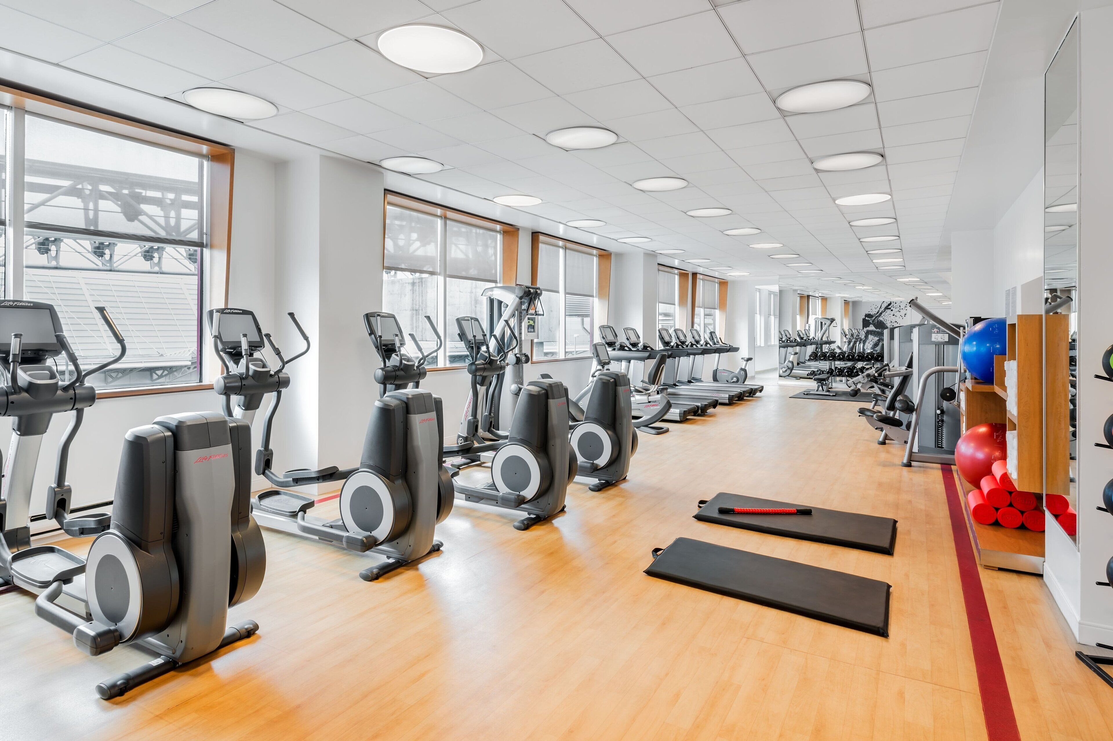 Un gimnasio con varias máquinas de cardio, bancos de pesas y pelotas de ejercicio.