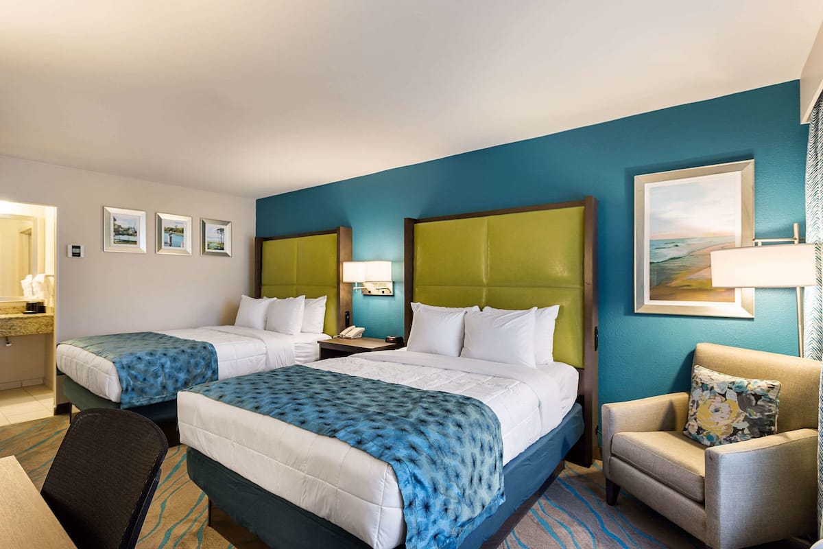 A hotel room with two beds, a chair, and a desk.