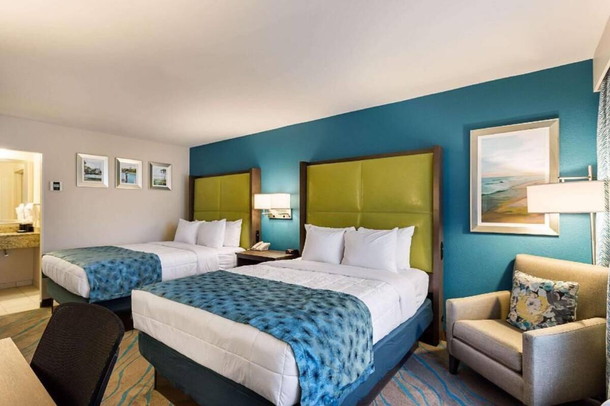 A hotel room with two beds, a desk, a chair, and a view of the ocean.