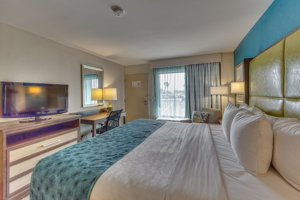 A hotel room with a bed, a desk, a television, and a window with curtains.