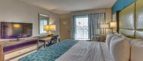 Una habitación de hotel con cama, escritorio, televisión y ventana con cortinas.