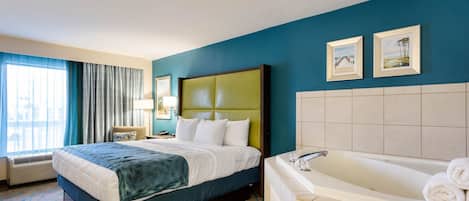 A hotel room with a large bed, a bathtub, and two framed pictures on the wall.