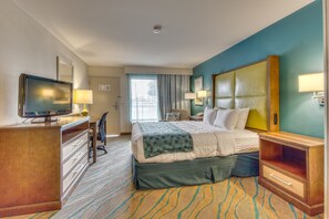A hotel room with a bed, desk, TV, and a view of the outside.