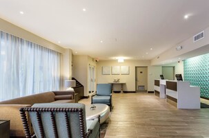 A hotel lobby with a reception desk, seating area, and a staircase.