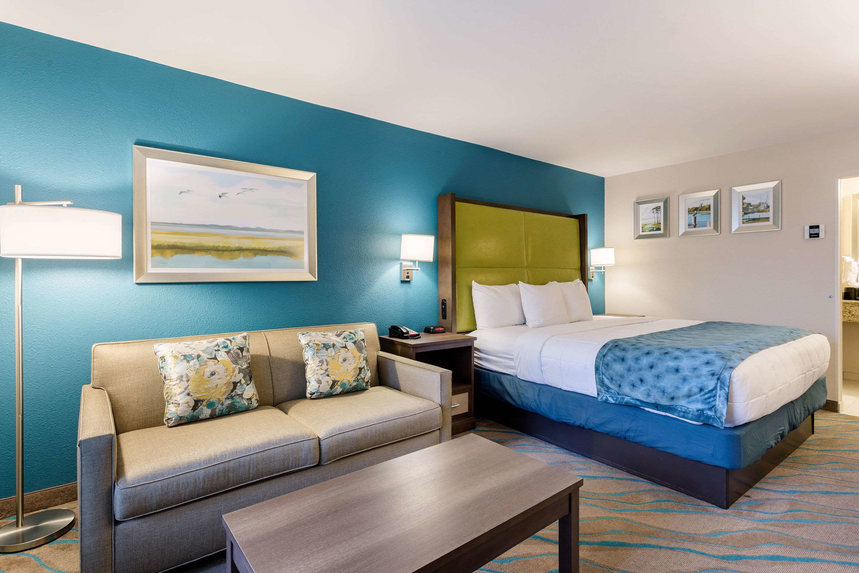 A hotel room with a bed, a sofa, a coffee table, and a painting on the wall.