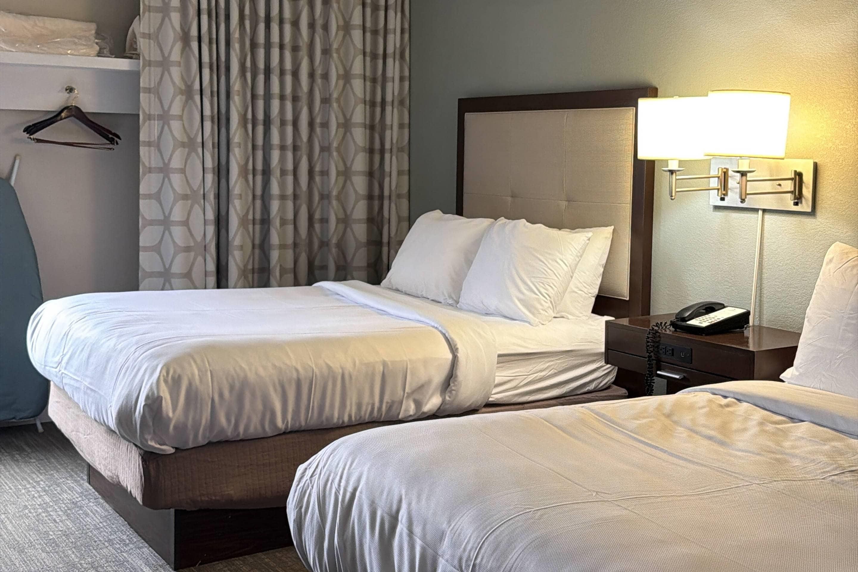 Habitación de hotel con dos camas, una mesita de noche con lámpara, un teléfono y un armario.