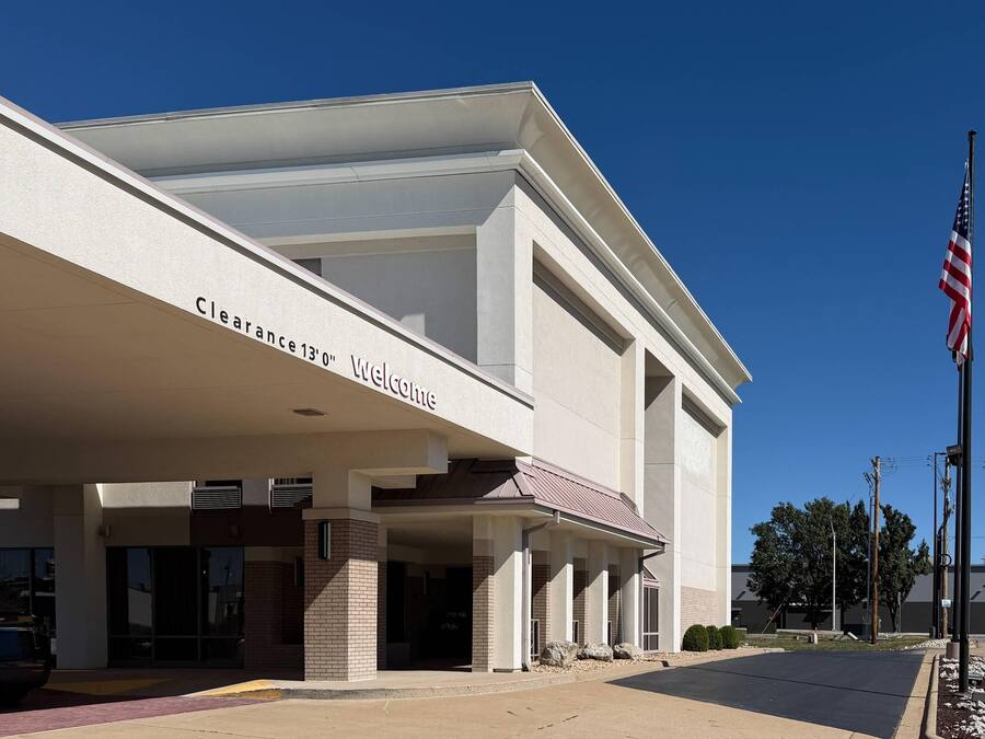 Un edificio con un cartello 'Clearance 13'0' Welcome', un'asta con la bandiera americana e un parcheggio.