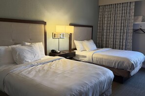 A hotel room with two beds, a bedside table with a lamp, a telephone, and a hanging coat rack.
