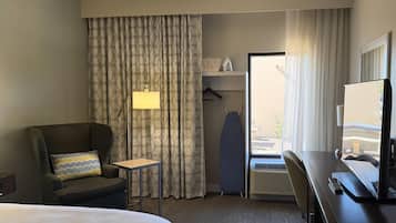 A hotel room with a bed, a desk with a computer, a chair, a lamp, a wardrobe, and a window with curtains.