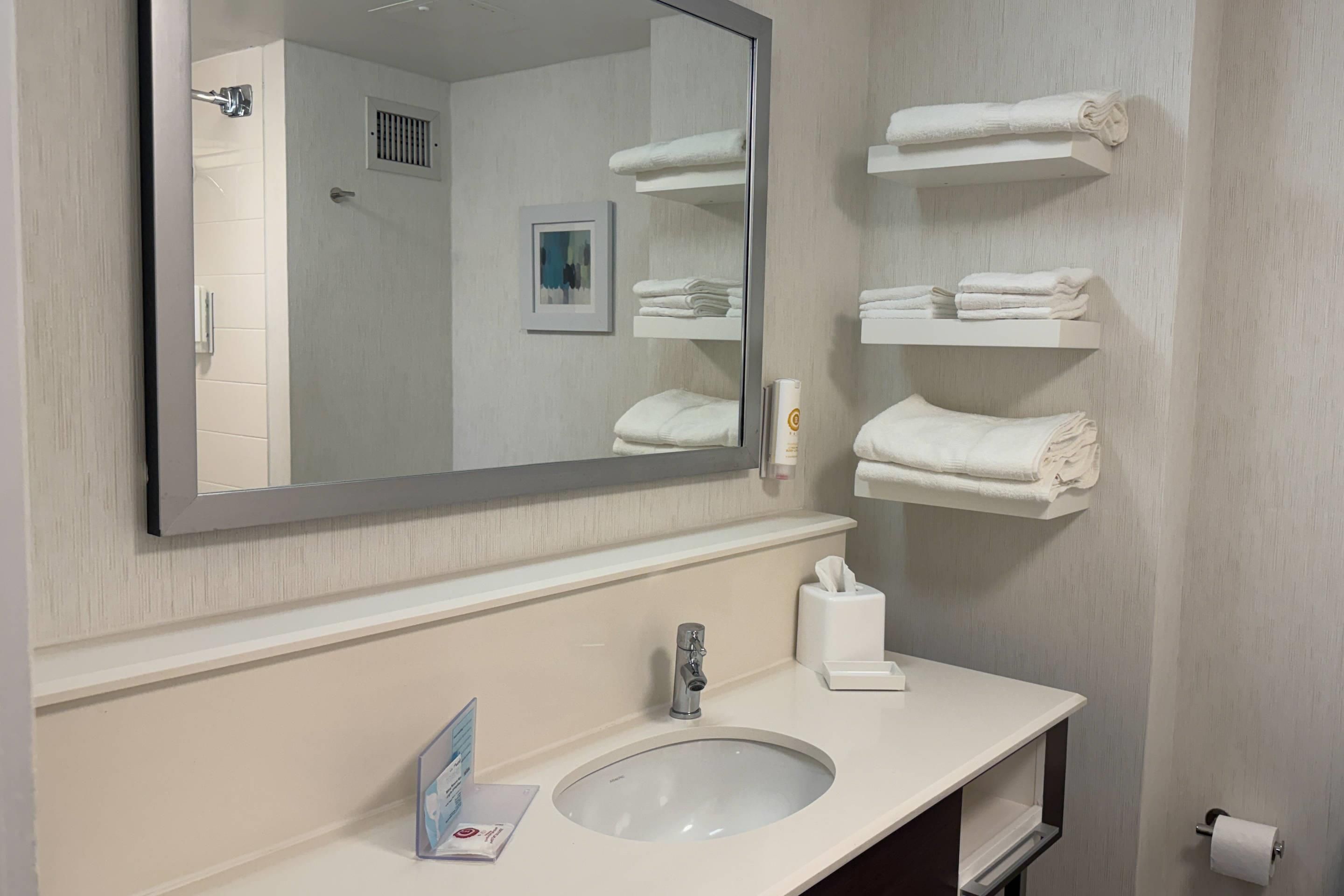 A bathroom with a large mirror, a sink, and shelves holding folded towels.