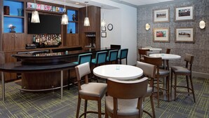 A bar area with a counter, multiple chairs, and tables. There are framed pictures on the wall and a clock. - Hampton Inn Louisville Downtown (Louisville)