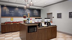 A breakfast bar with a chalkboard menu, a microwave, and various food and drink dispensers. - Hampton Inn Louisville Downtown (Louisville)