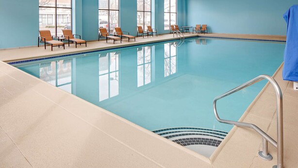 An indoor swimming pool with clear blue water, surrounded by lounge chairs and large windows. - Hampton Inn Louisville Downtown (Louisville)