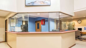 Un área de recepción con un separador de vidrio, una puerta de madera y un reloj en la pared.