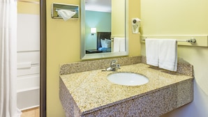 Un baño con lavamanos de encimera de granito, espejo, toallero y cortina de ducha.