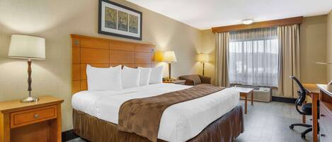 Habitación de hotel con una cama grande, dos mesitas de noche con lámparas, un escritorio con una silla y una ventana con cortinas.
