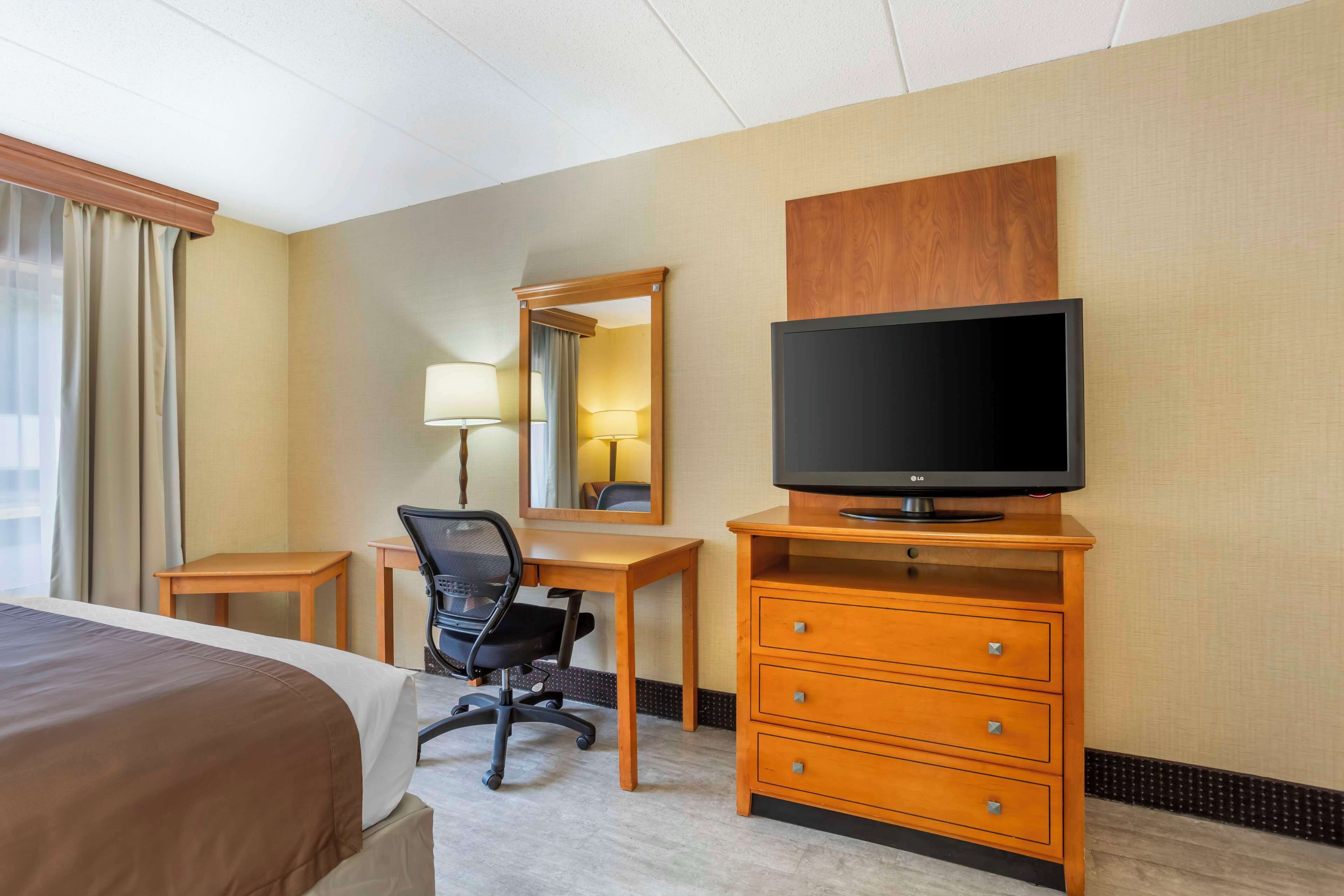 A hotel room with a bed, a desk with a chair, a television, and a dresser.