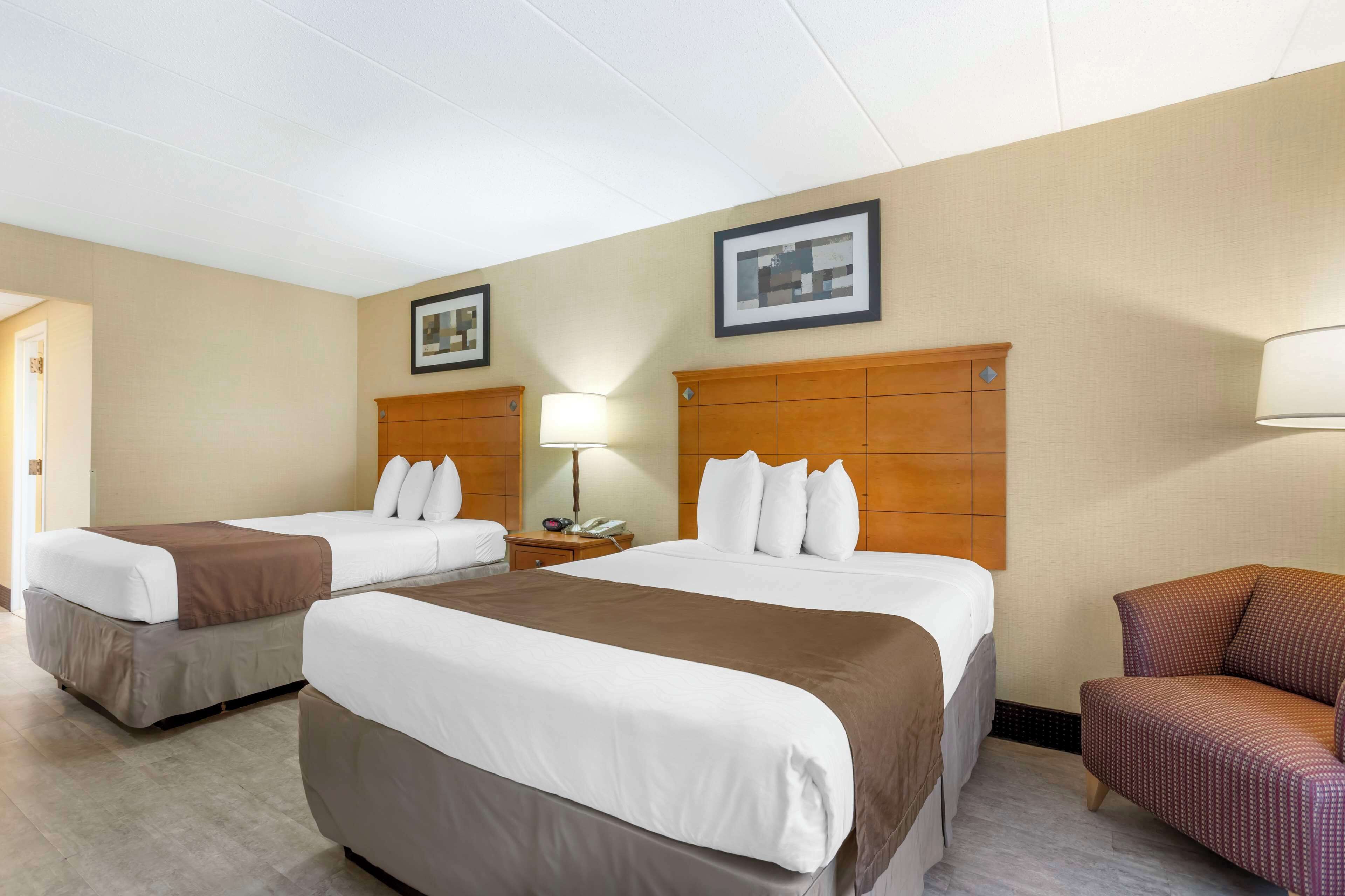 A hotel room with two beds, a nightstand, a lamp, a chair, and framed pictures on the wall.