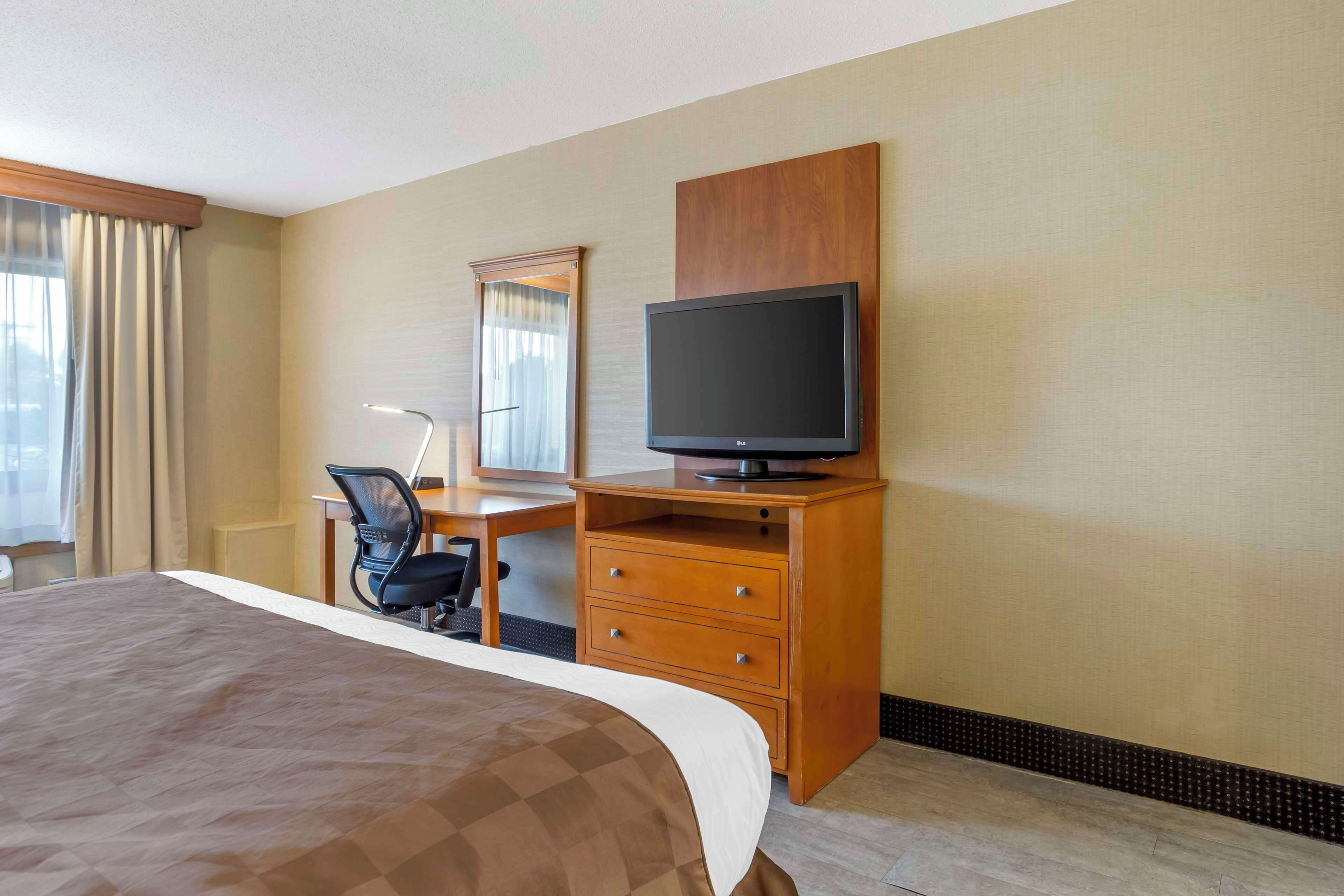 A hotel room with a large bed, a desk with a chair, a television, and a mirror.