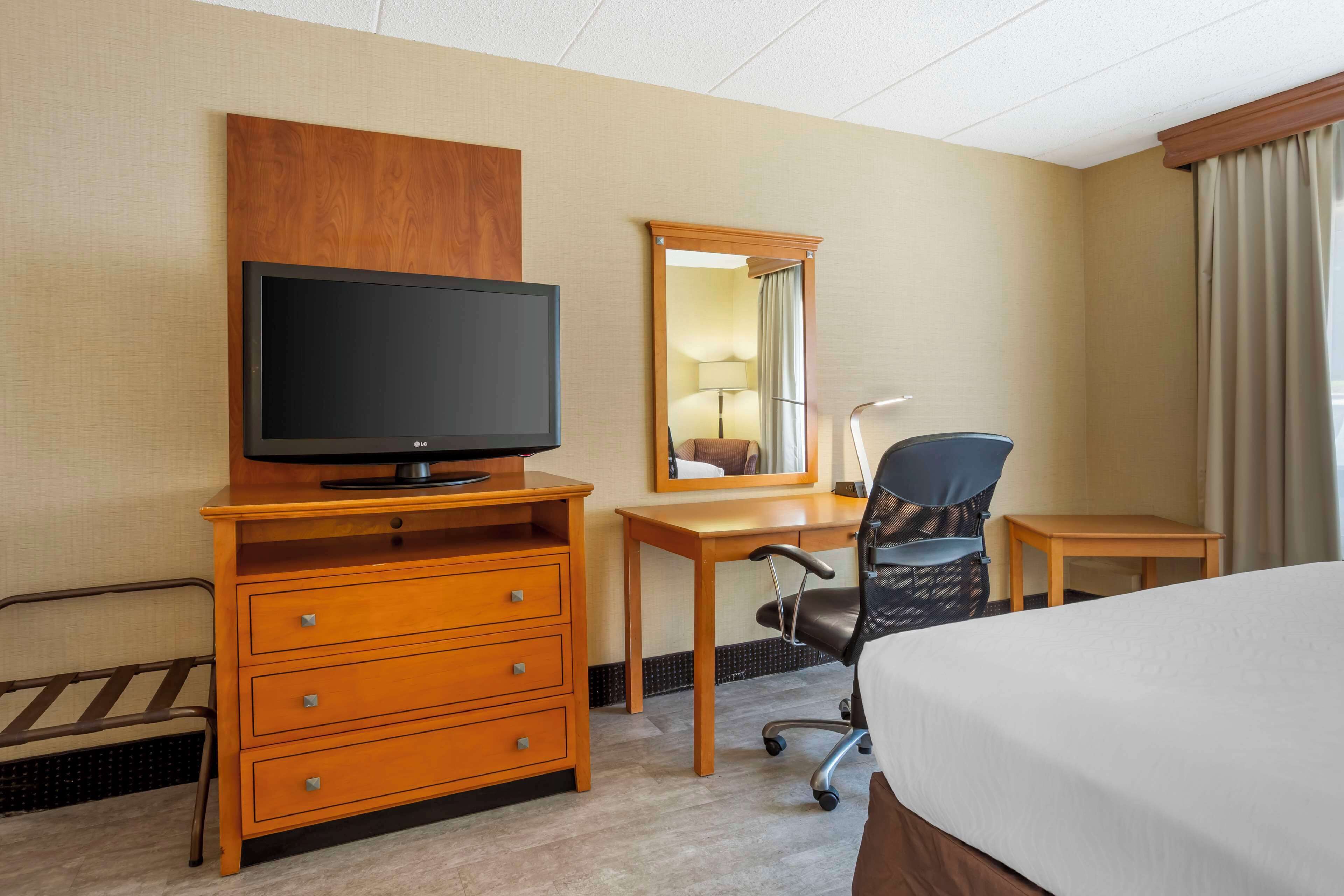 A hotel room with a bed, a desk with a chair, a television, a dresser, and a mirror.