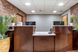 Un área de recepción con dos mostradores, pared de ladrillo y plantas en macetas.