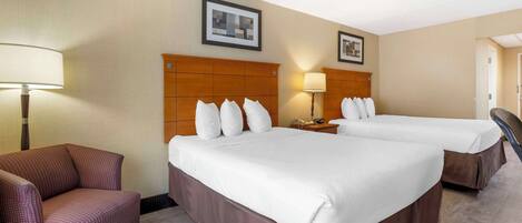A hotel room with two beds, a sofa, a nightstand with a lamp, and framed pictures on the wall.
