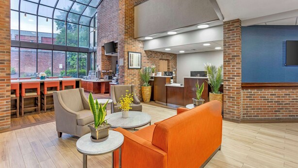 A modern lobby with a high ceiling, brick walls, and a glass enclosure. There are seating areas with tables and chairs, and a kitchen area in the background. - Best Western Danbury/Bethel (Bethel)