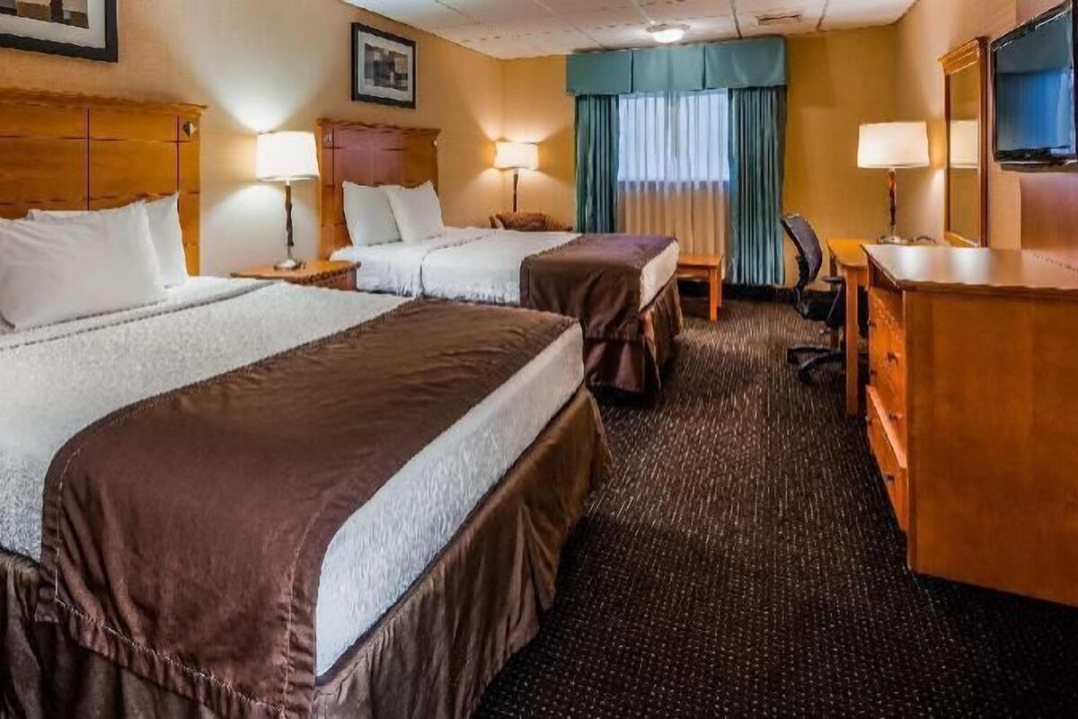 A hotel room with two beds, a desk, a chair, a TV, and a window with curtains.