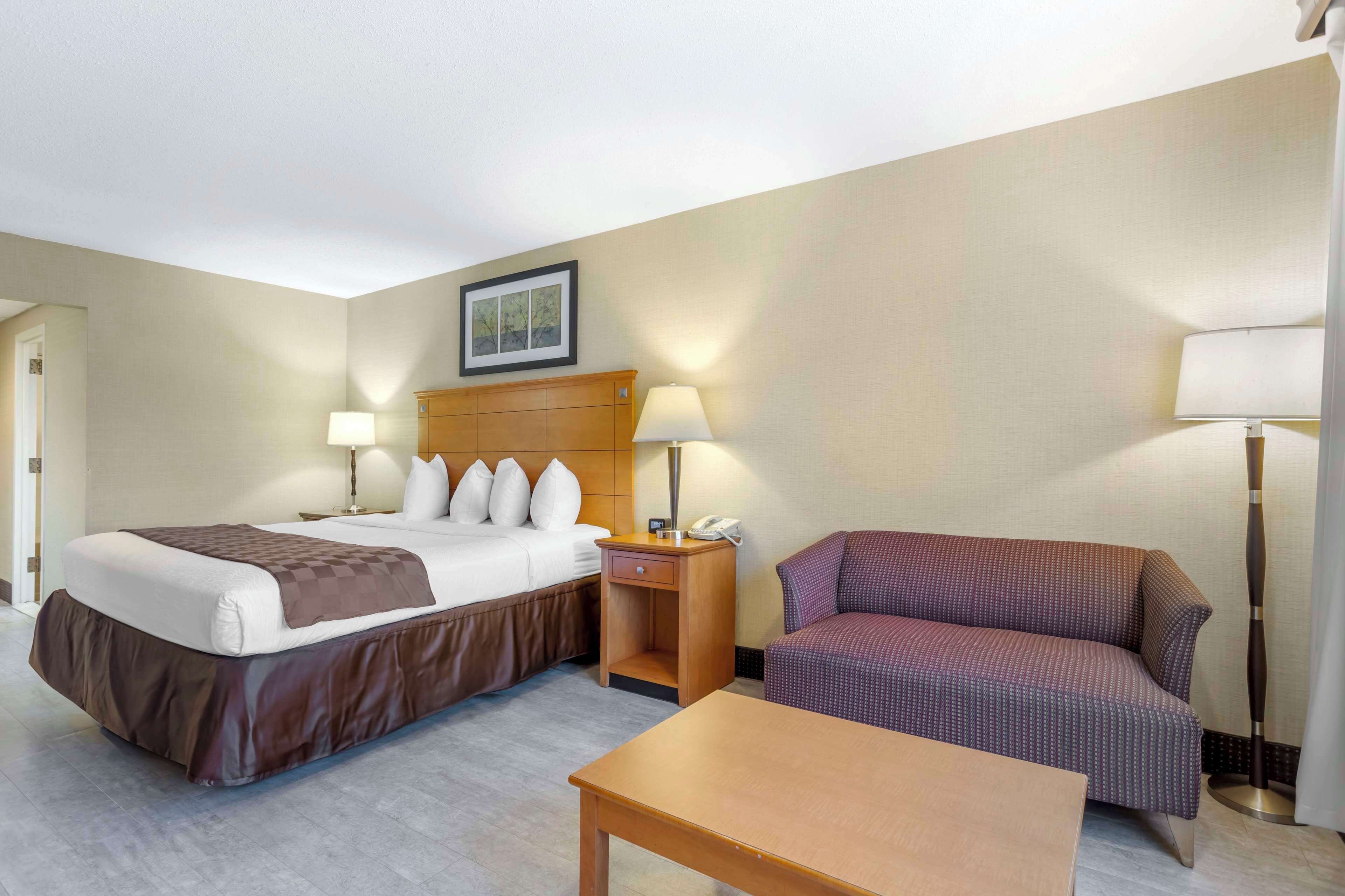 A hotel room with a large bed, two bedside tables with lamps, a small table, and a sofa.