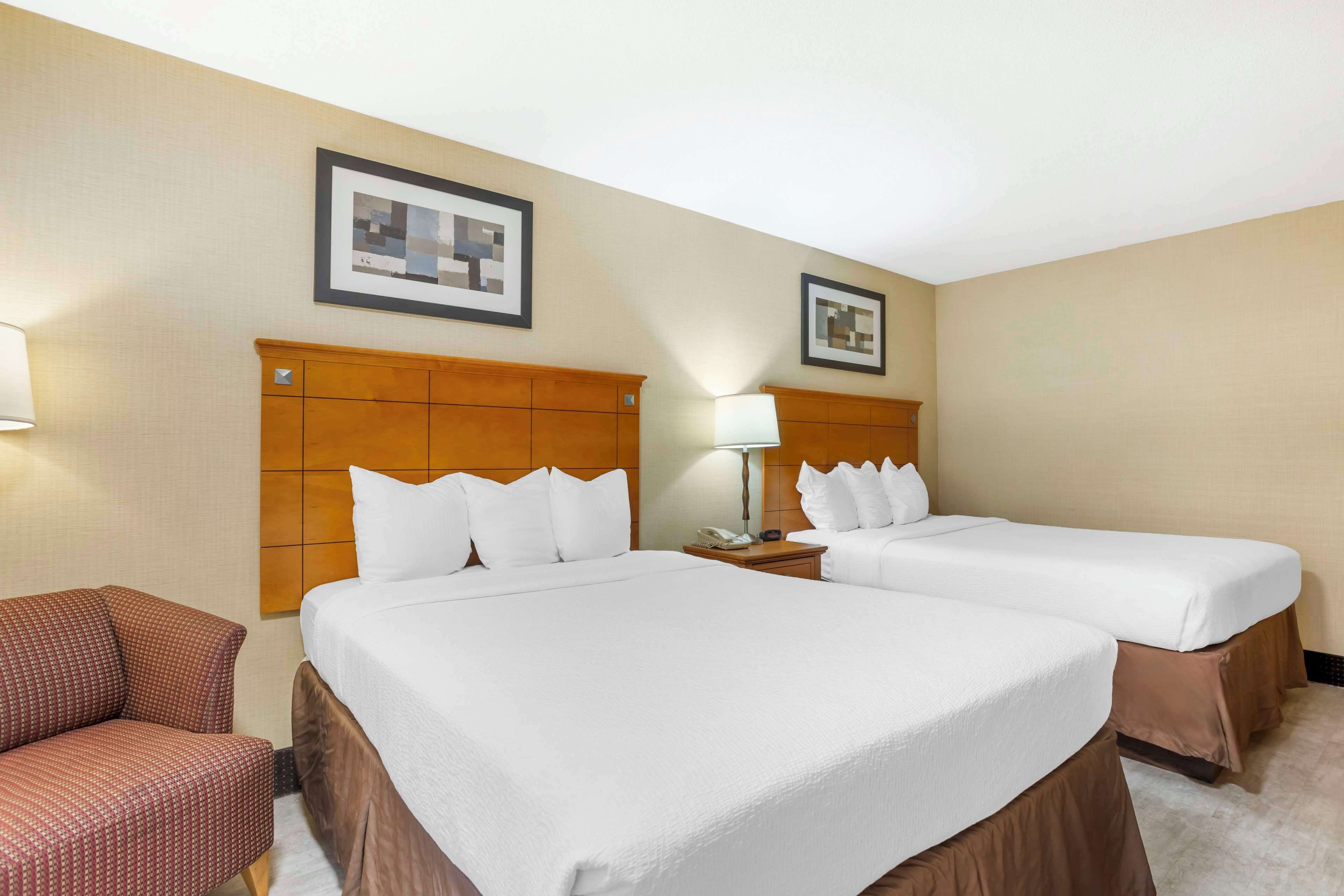 Quarto de hotel com duas camas, uma cabeceira de madeira, uma poltrona vermelha e duas fotos emolduradas na parede.