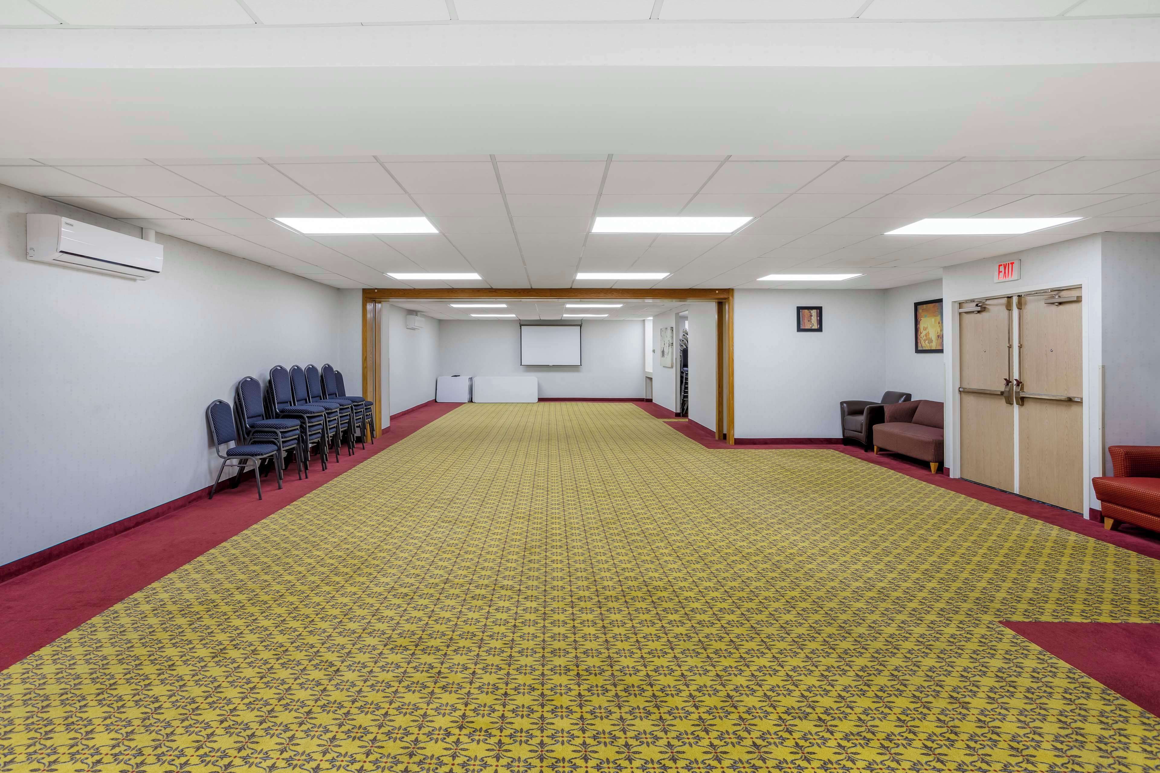 A conference room with a patterned carpet, rows of chairs, a whiteboard, and an air conditioning unit.