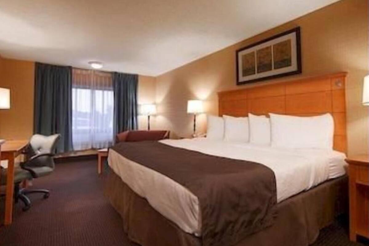 A hotel room with a bed, desk, chair, and a painting on the wall.