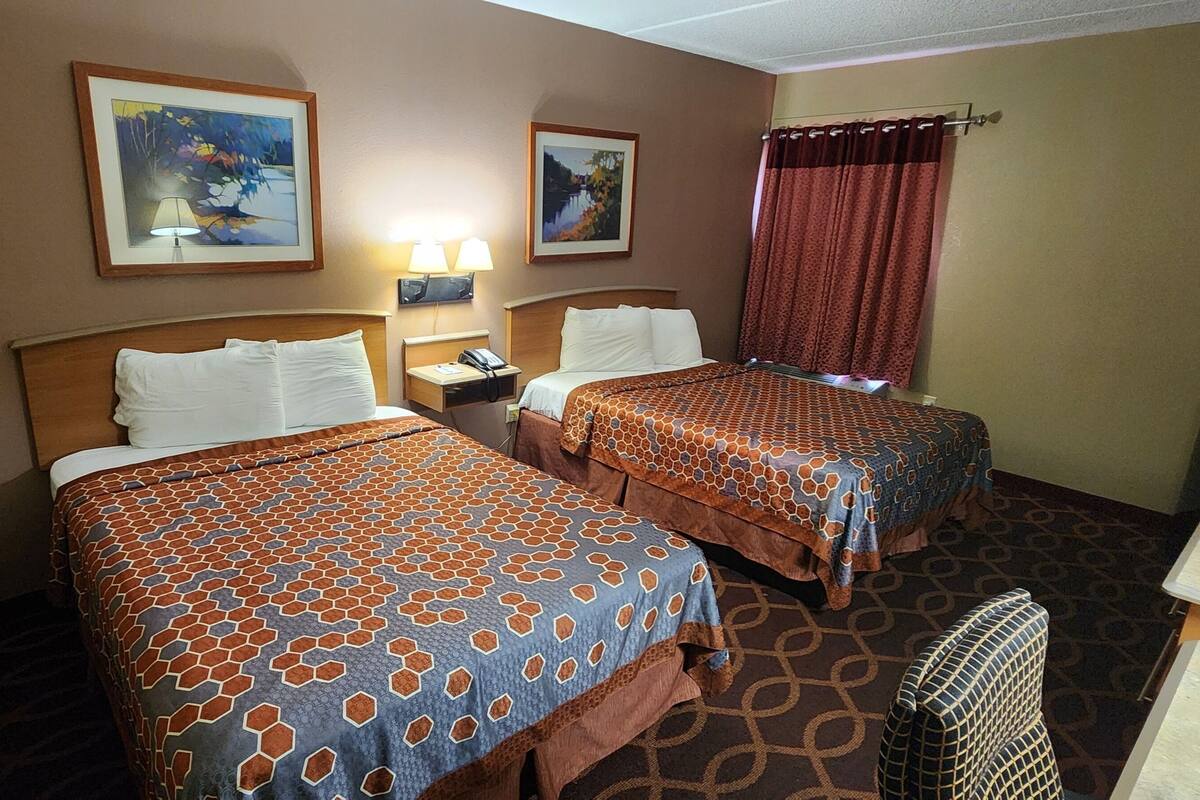 A hotel room with two beds, a desk, a chair, and two lamps.