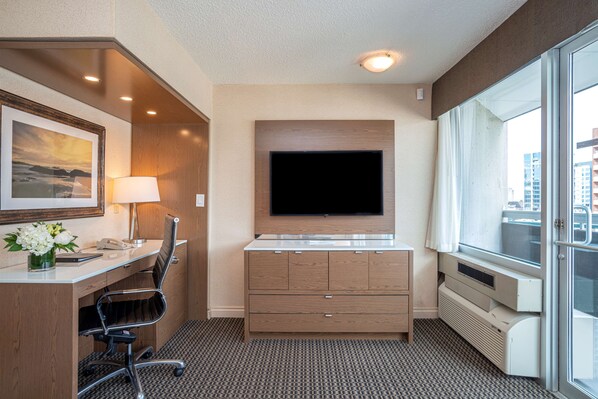 Habitación de hotel con escritorio, silla, televisión y un ventanal grande.