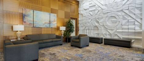A lobby with a wooden panel wall, a gray sofa set, a large abstract wall art, and a patterned carpet.