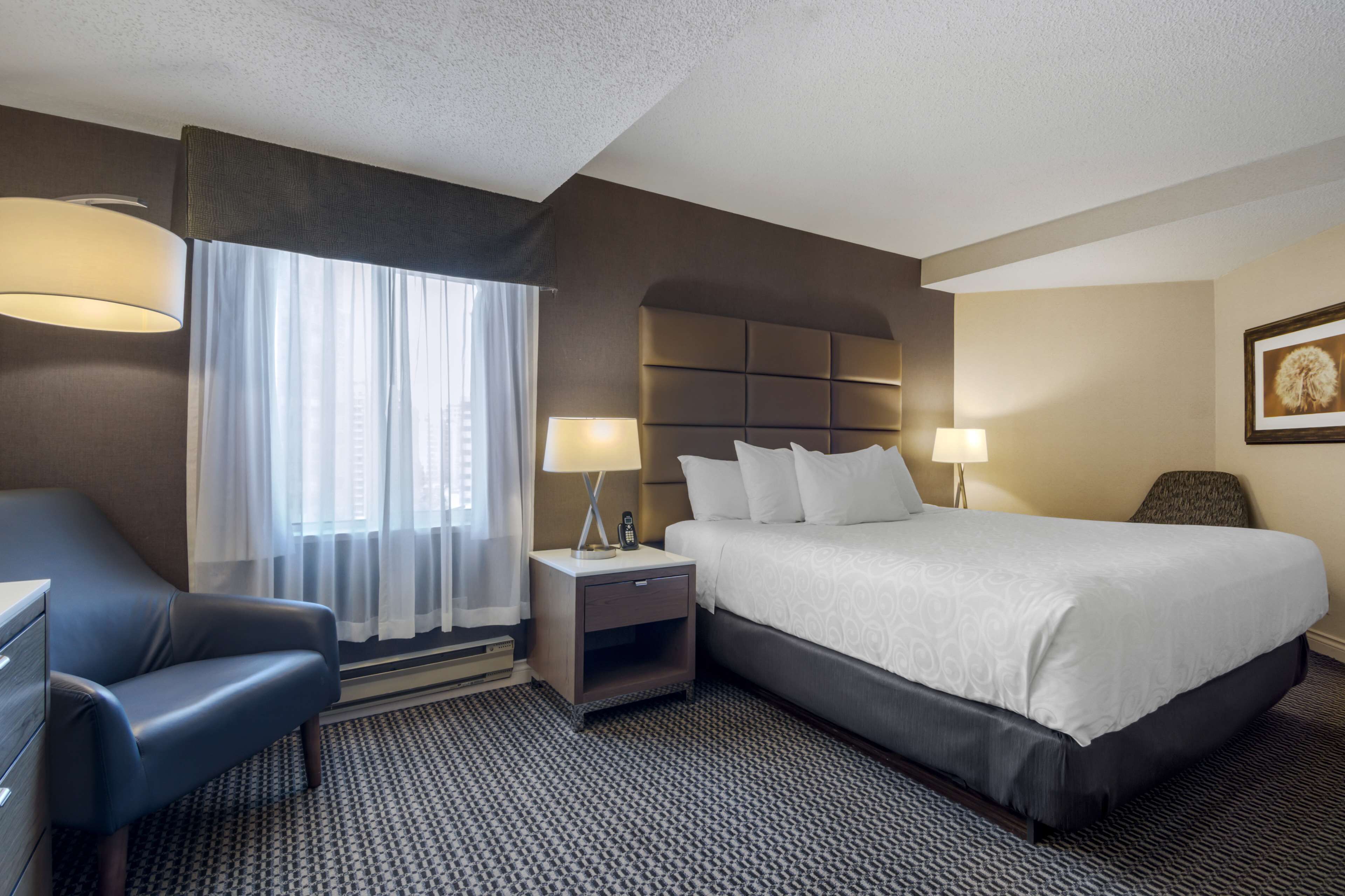 A hotel room with a bed, a desk, a chair, a nightstand, and a lamp.