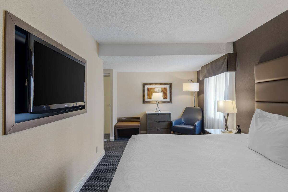 Ein Hotelzimmer mit einem großen Bett, einem flachbildfernseher an der Wand, einem Schreibtisch mit Stuhl und einer Lampe.