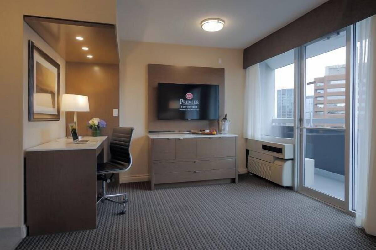 Ein Hotelzimmer mit Schreibtisch, Stuhl, Fernseher und einem großen Fenster.