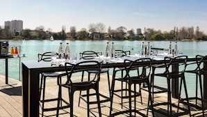 A dining area with a table set for four, overlooking a calm body of water with a boat in the distance.